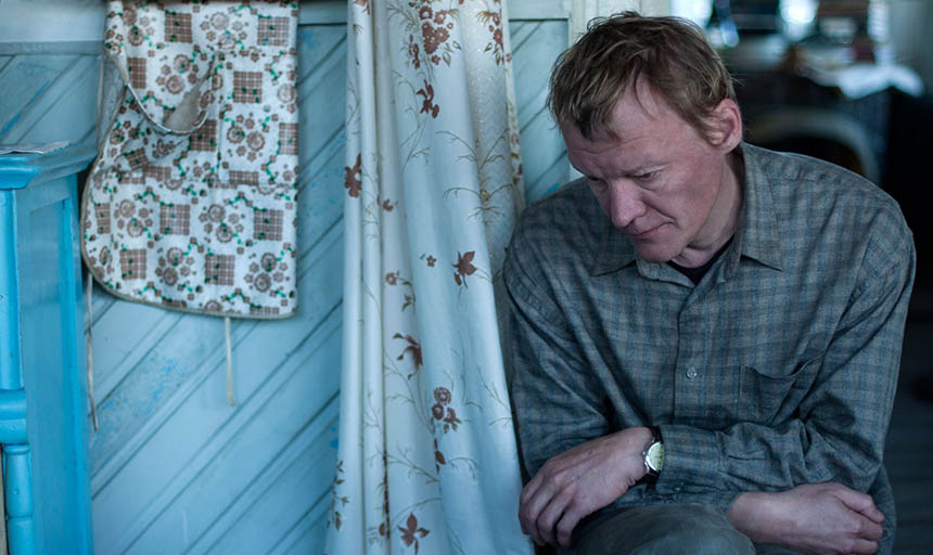 An actor crouching down next to a blue door