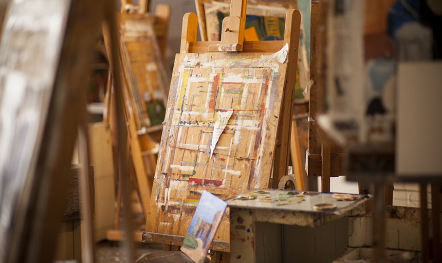 An easel in a crowded art room with a painting on it