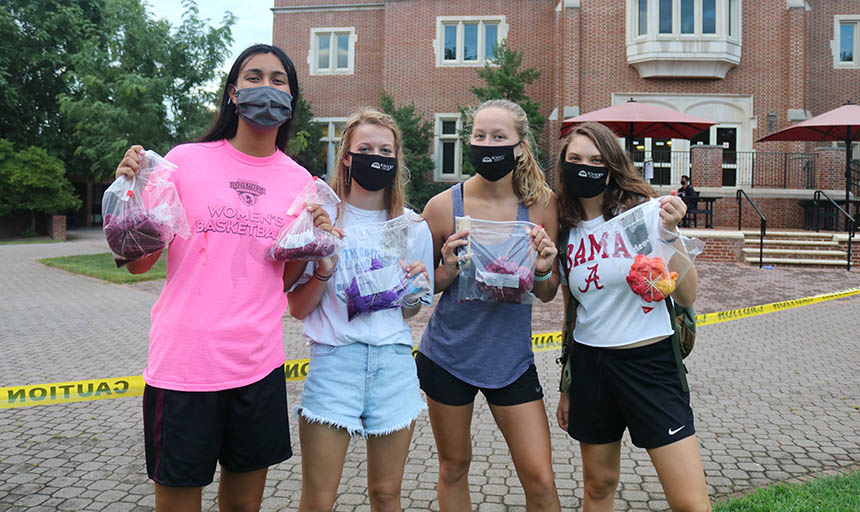 Masked students holding up their tie dye creations in bags