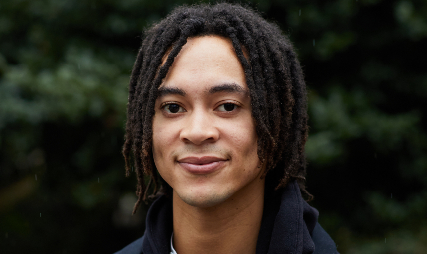 Headshot photo of Sandy Williams IV, they have black hair in dreads and they're smiling at the camera. 