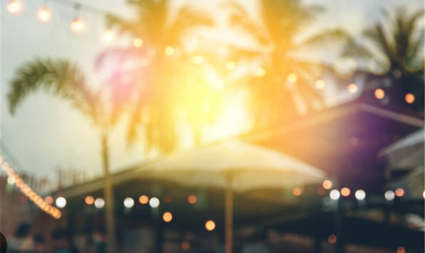 blurred image of a beach setting with palm trees, string lights, and sunset
