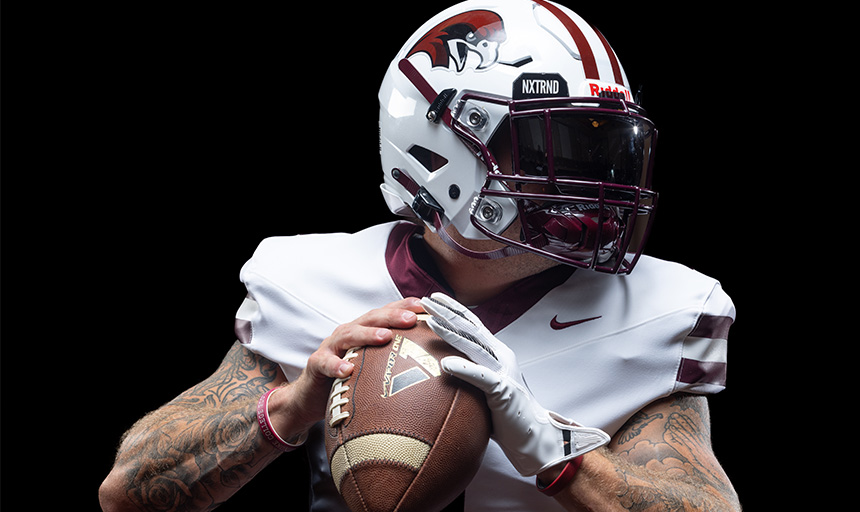 A football player in uniform grasps a football in his hands