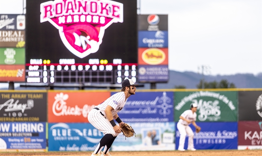 baseball player on the field with Roanoke Maroons logo behind him