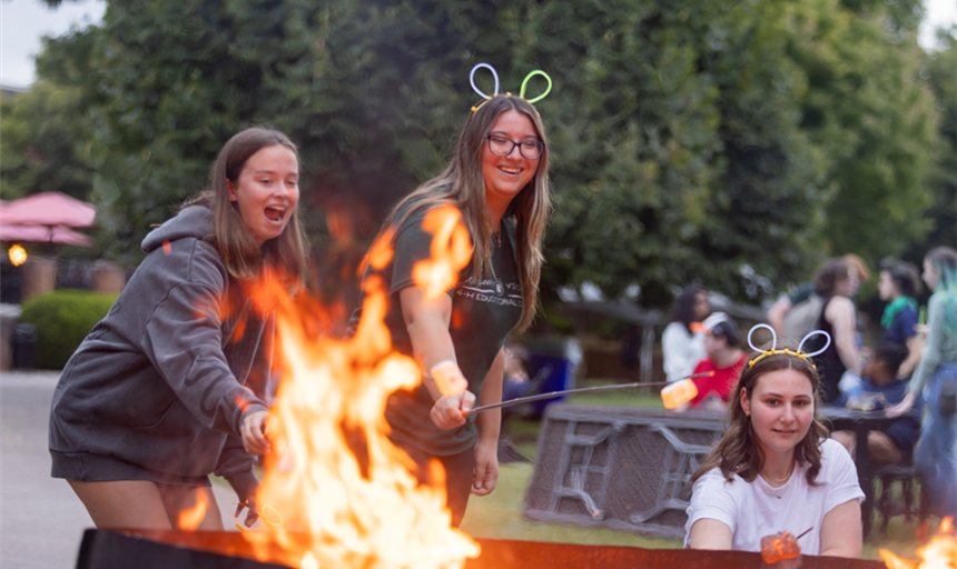 three students making s'mores at a bonfire