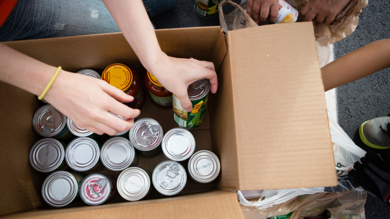 Closeup of hands boxing up canned food donations