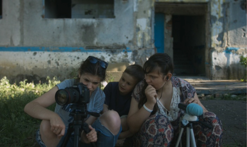 Three people crouched together while working with a film camera