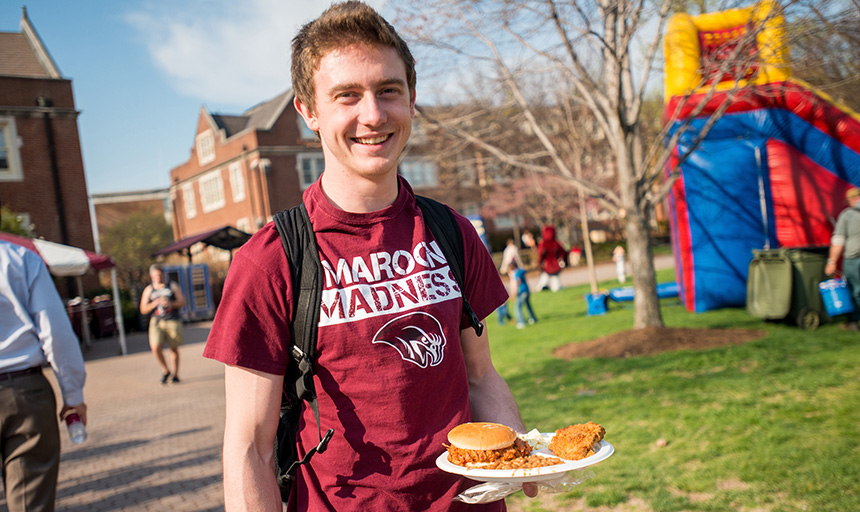 A student smiling and holding a plate of food on the quad