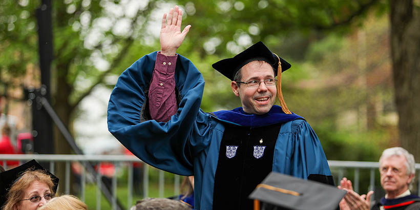 Chris Lassiter standing and raising a hand at commencement