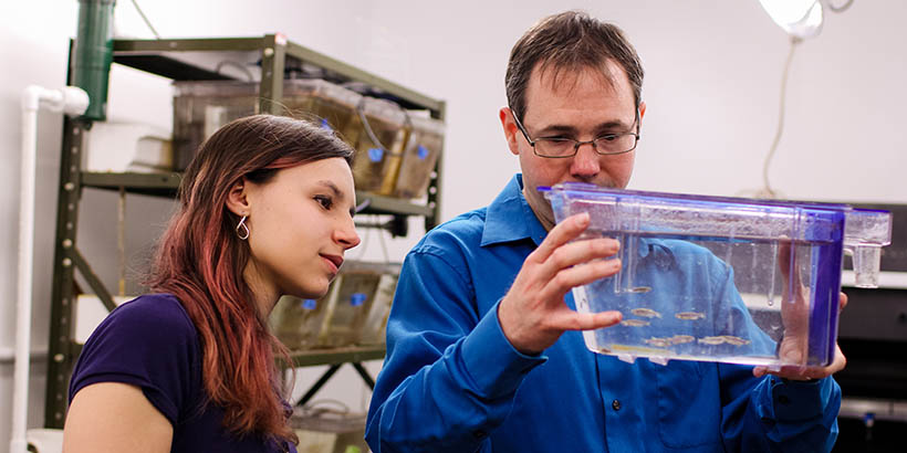 Chris Lassiter holding a fish tank and looking at it with a student