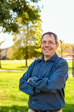 Chris Lassiter standing on the back quad with arms crossed