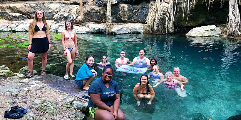 Students at a natural water pool with a Roanoke College banner