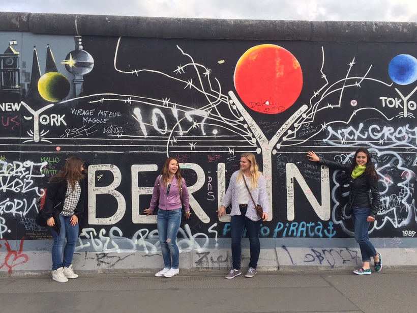 Students standing in front of a wall decorated with art and the word "Berlin" in large letters