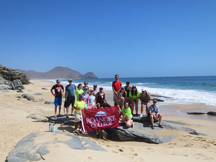 Students holding a roanoke college flag on a beach in Mexico