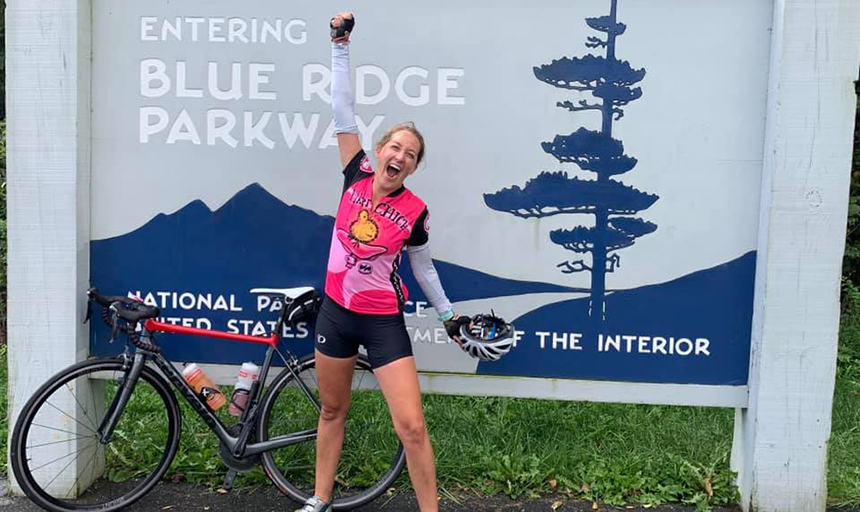 Woman yells in triumph next to bike and Blue Ridge Parkway sign