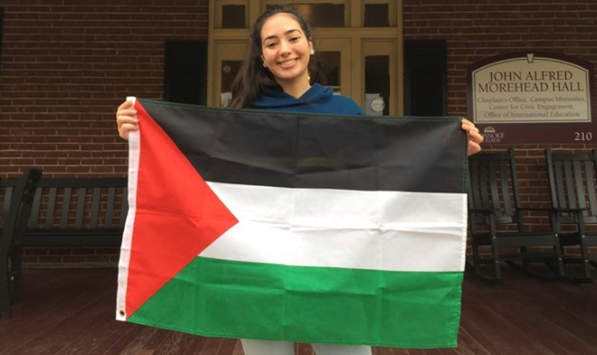 Female student standing on porch of campus building with Palestinian flag