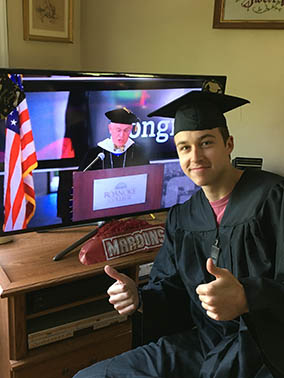 A graduate in a cap and gown smiling next to the livestream