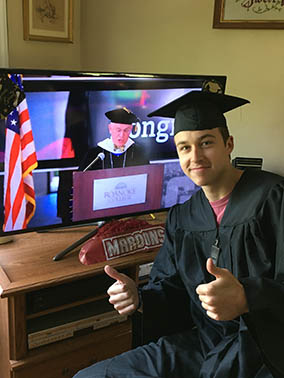 A graduate in a cap and gown smiling next to the livestream