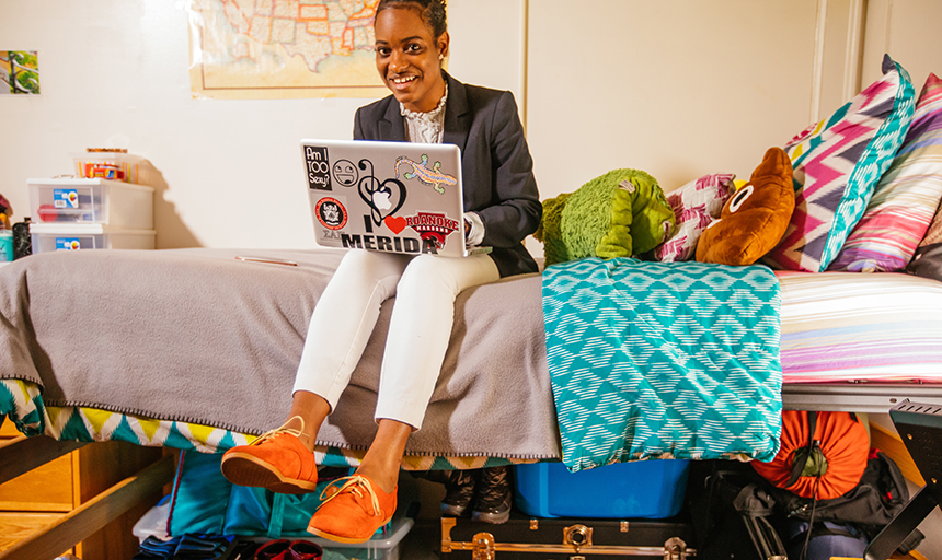 student sits on bed while holding laptop