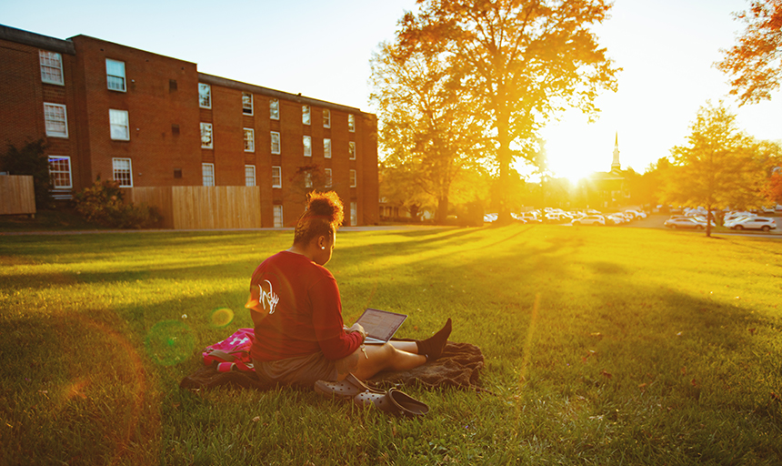 Student working on laptop outside during fall sunset