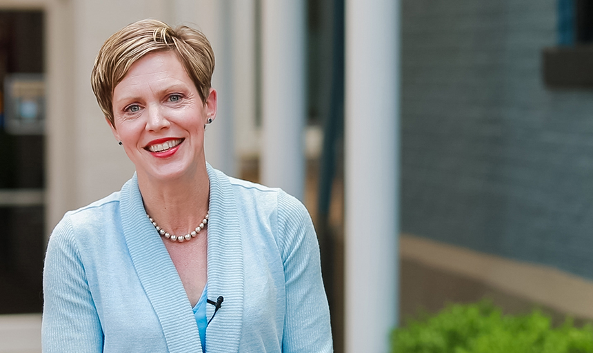 Dr. Alice Kassens portrait in a light blue cardigan with white columns in the background