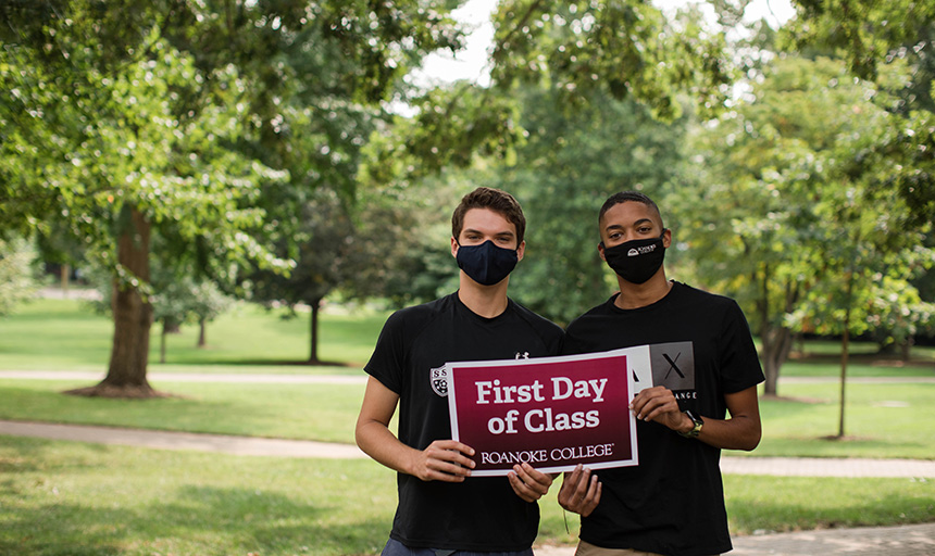 two students wearing masks holding First Day of School sign