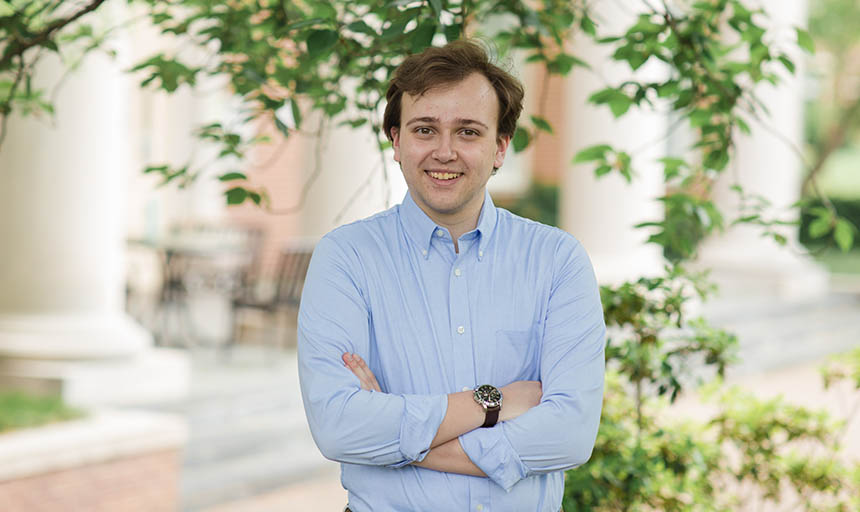 Hunter Haskins standing in front of a building on campus and a tree