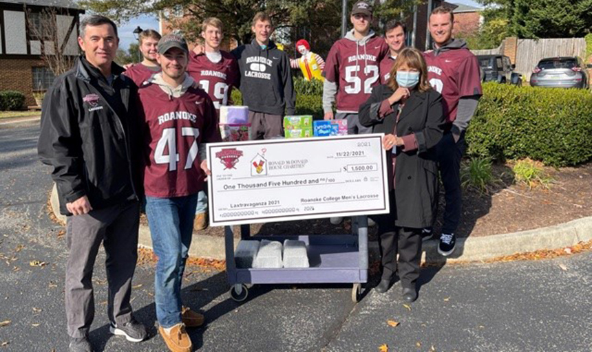 Men's Lacrosse Team stands with Ronald McDonald House representative holding a large check