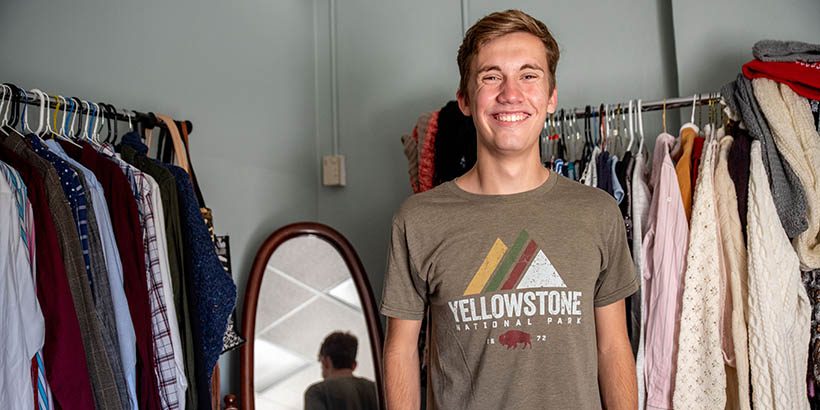 A student standing in front of racks of clothing and smiling