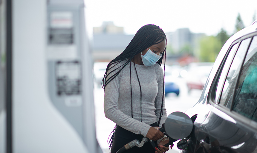woman in facemask at gas station filling up car