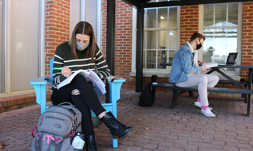 Two students wearing face coverings do homework outside