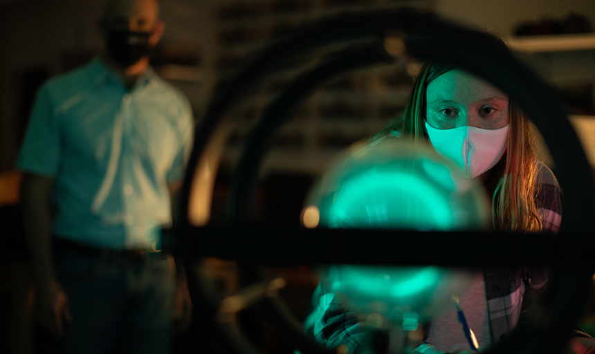 Student takes notes in science lab by glowing green light in circular equipment