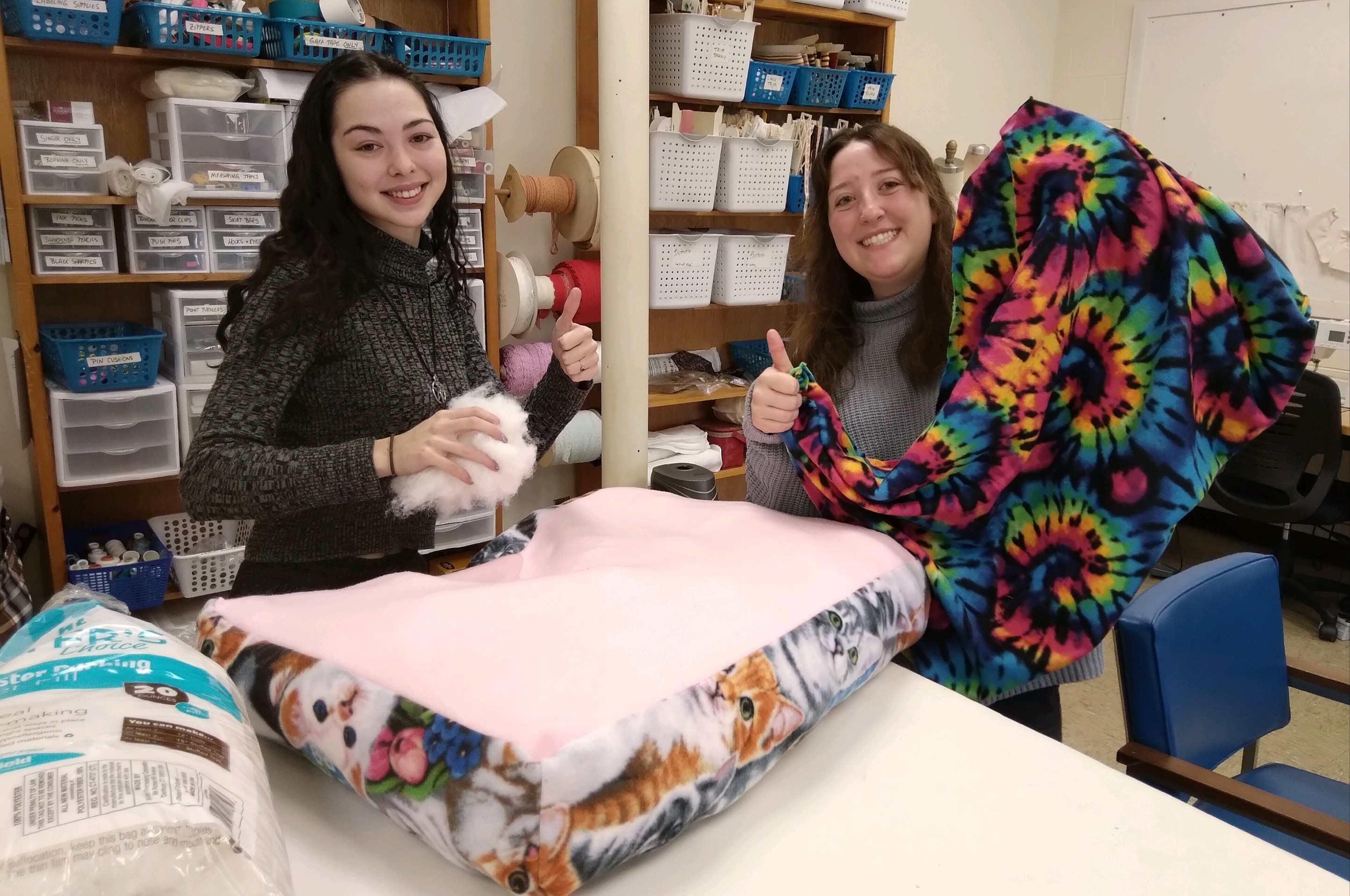 Two students hold up pet beds they sewed