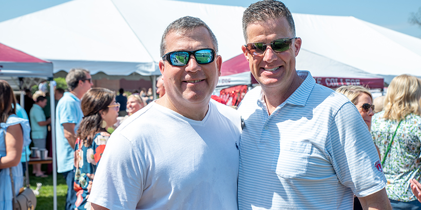 two people standing together both wearing sunglasses with crowd in background