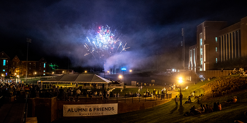 Fireworks are shown above a crowd of people and a sign saying Welcome Alumni and Friends
