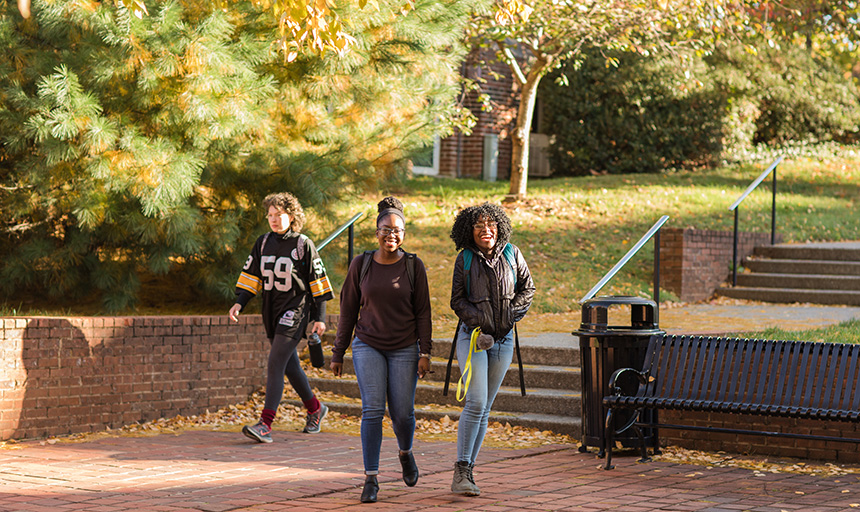 Three students walk on brick staircase and patio. two are walking toward camera. 