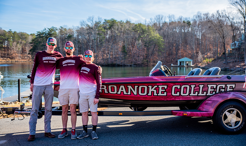 Three fishermen in Roanoke bass fishing jerseys pose in front of Roanoke fishing boat