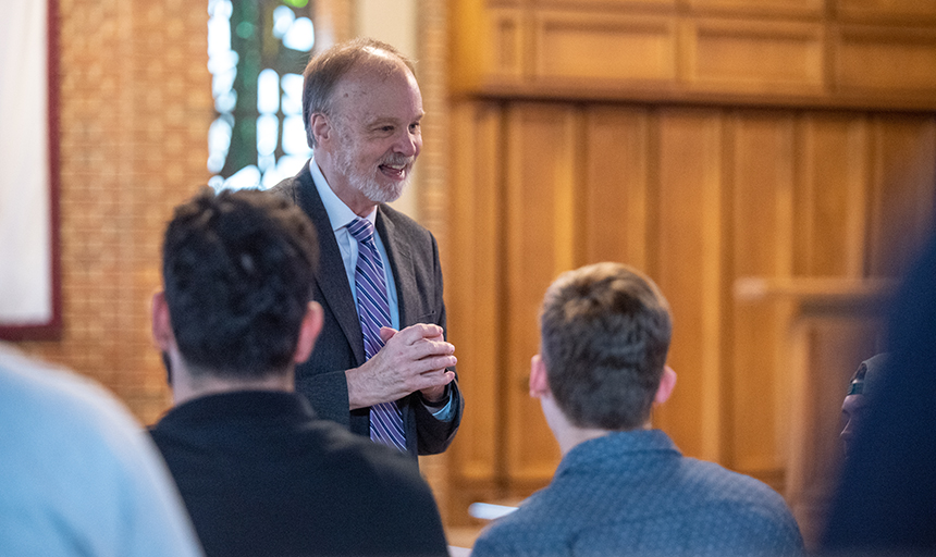 Smiling man in suit speaks to students in chapel