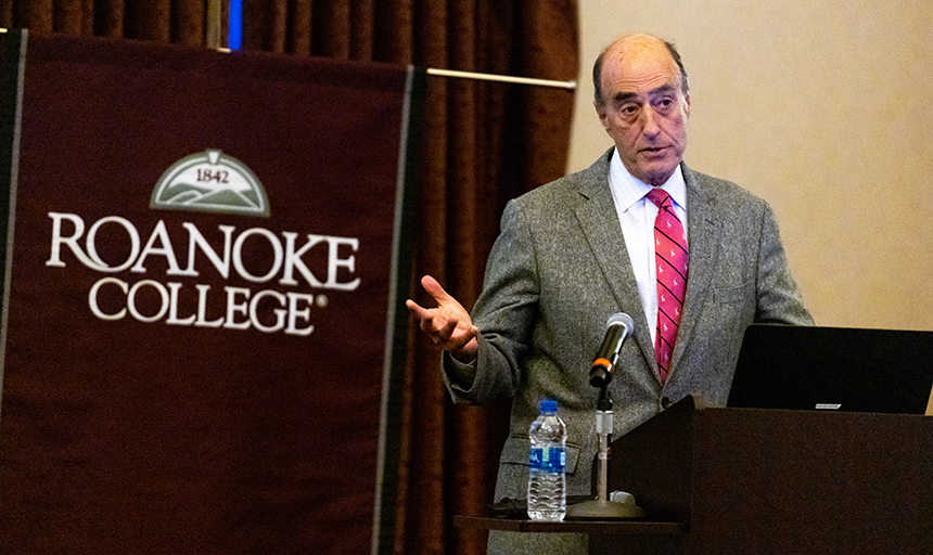 Robert Fabrikant speaks at podium with Roanoke College banner behind him