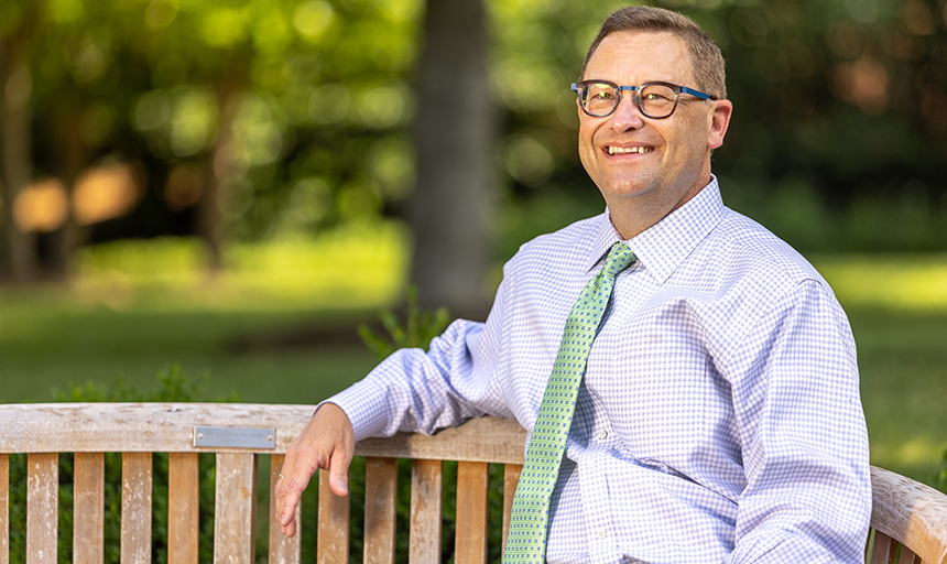 Frank Shushok leaning on a bench smiling to camera