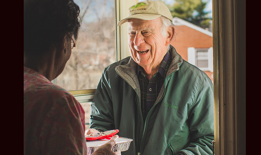 George Kegley hands food to person at the left for Meals on Wheels
