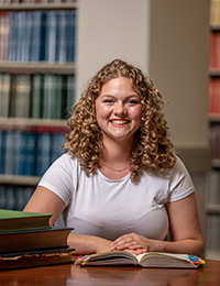 young woman pictured in library with books on table and on shelves around her