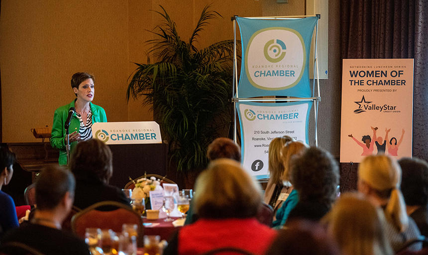 Professor talks at podium by Chamber of Commerce sign