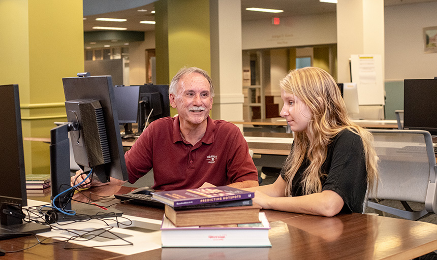 Professor and student sit at computer in library