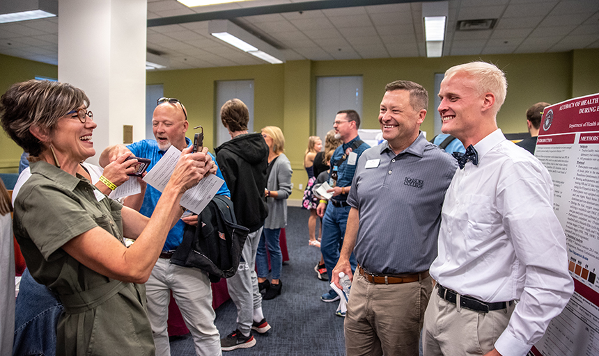 Kelly Shushok snaps a photo of her husband, President Frank Shushok Jr., with a student during the Family Weekend research showcase in Fintel Library.