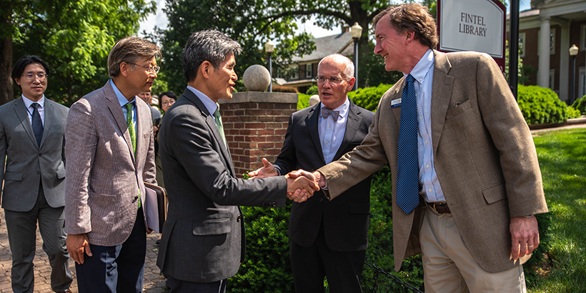 Two men shake hands as others watch on