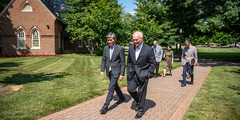 Two men walk on campus with others behind them