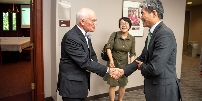 Two men shake hands as a woman watch on