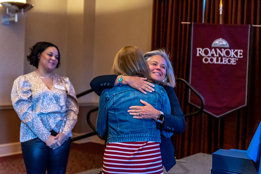 women hug in front of Roanoke College banner