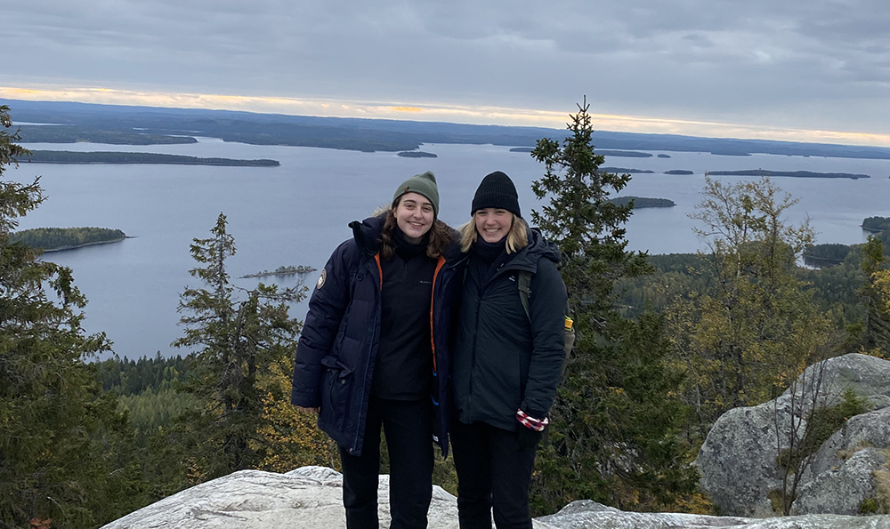 two young people pose on mountain near water