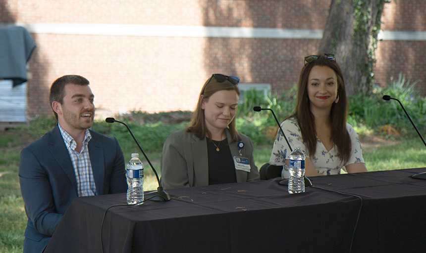 One man and two women speak outdoors at microphones